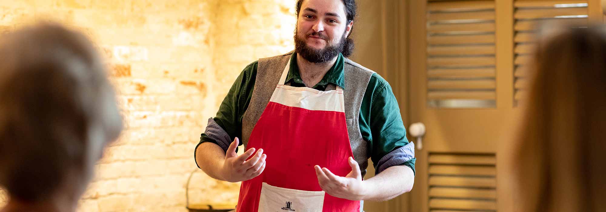 A man in an apron talks to a group of visitors.