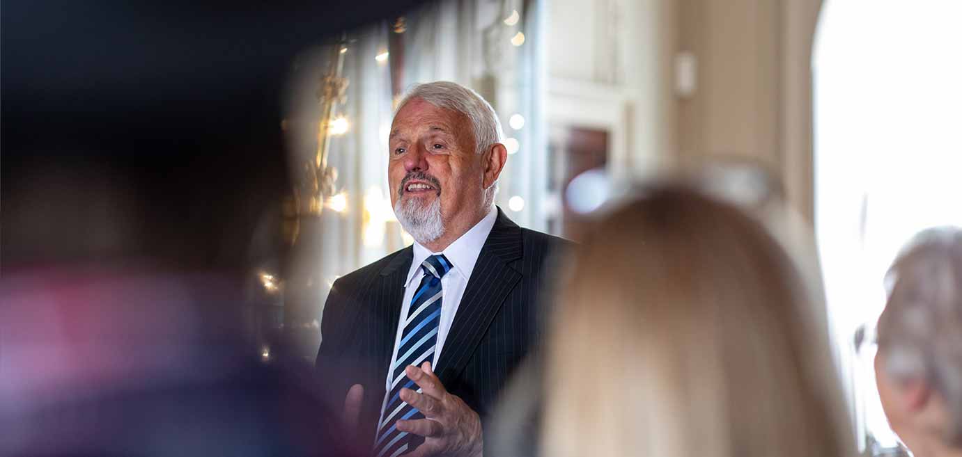 A man in a suit explains something to a group of visitors