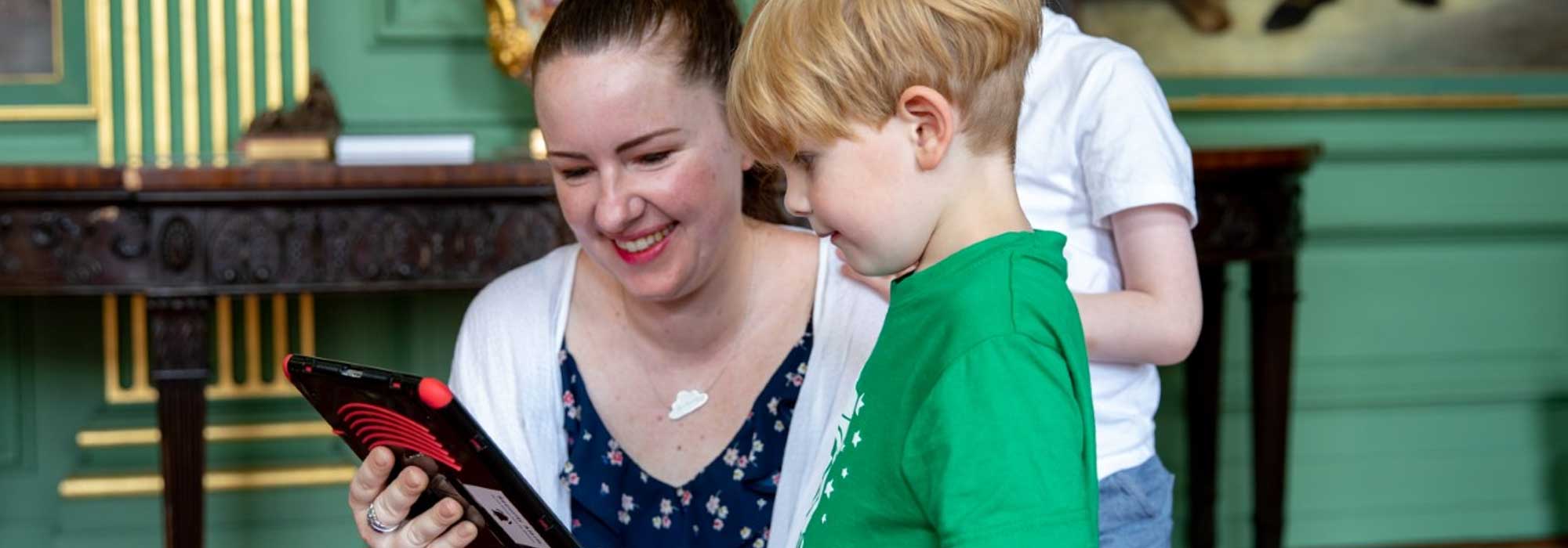 A lady is showing a little boy something on a tablet device and both are smiling