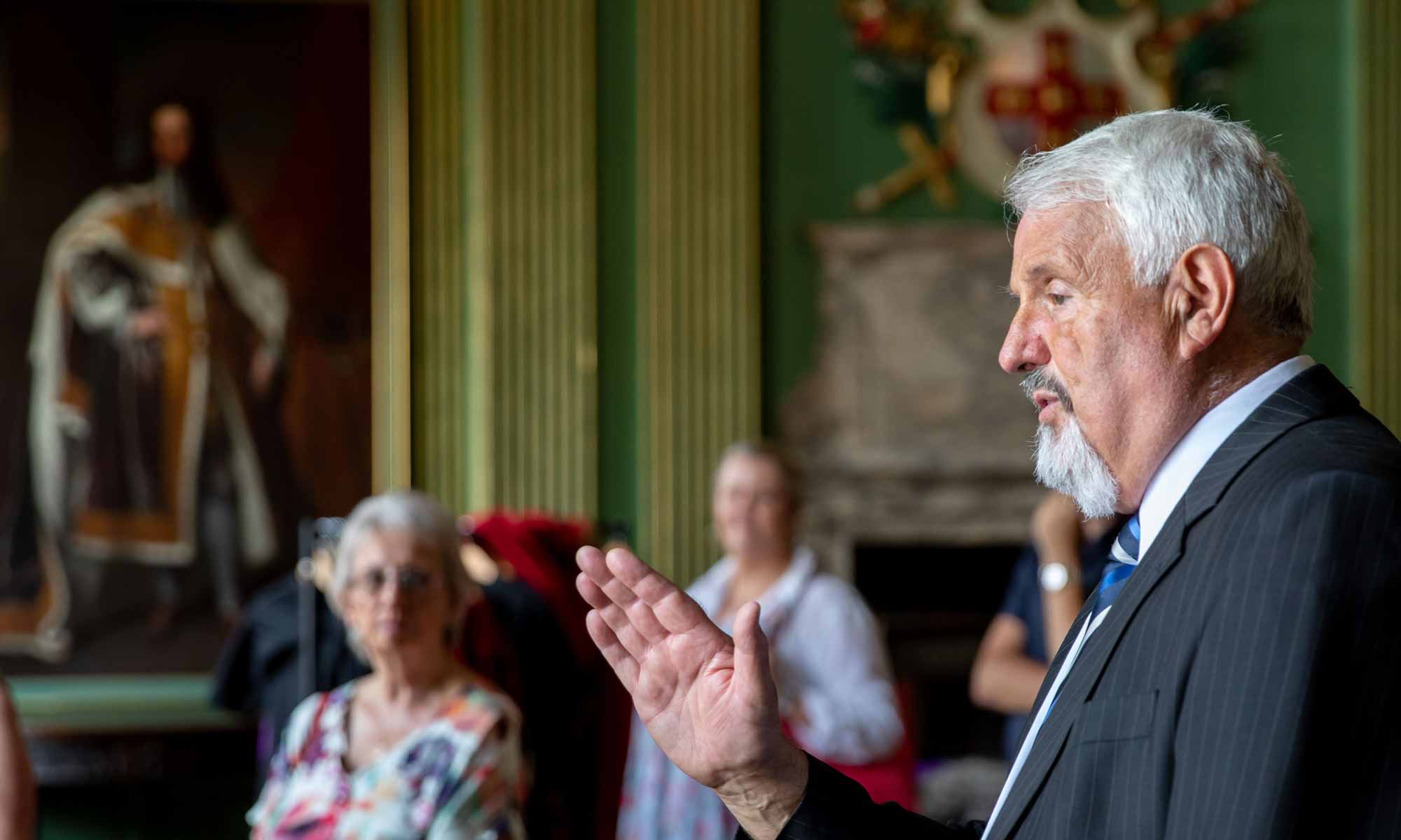 A gentleman in a suit talking to a group of people in the State Room.