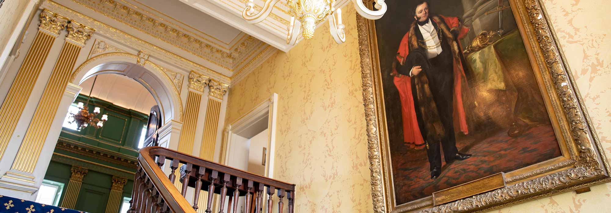 A view of a staircase inside the Mansion House in which a large portrait is hung alongside one wall