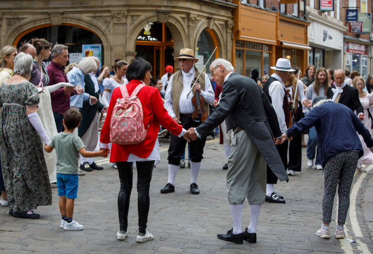 A circle of people hold hands interspersed with people in Georgian costumes