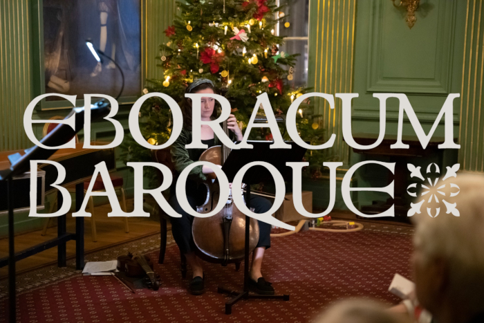 Woman playing a Cello in front of a decorated Christmas tree for an audience with the text "Eboracum Baroque" over the image in white.