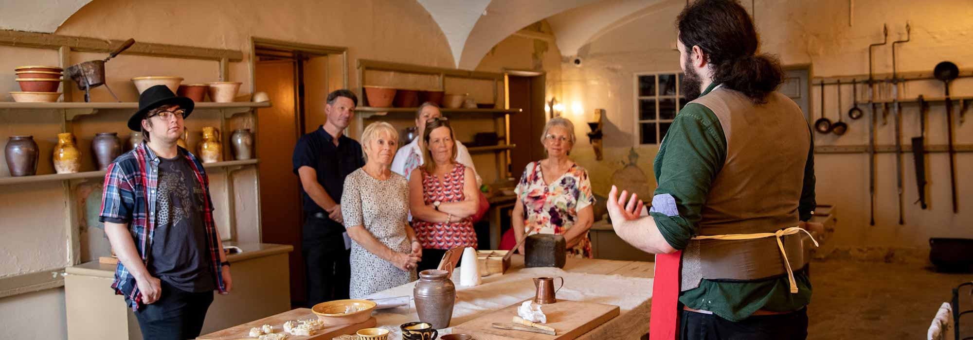 A group of visitors listen to a talk by a man in an apron in the Mansion House kitchen.