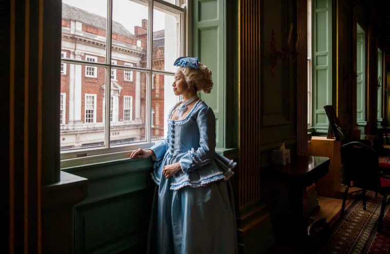 A lady in a blue Georgian costume looks out a window