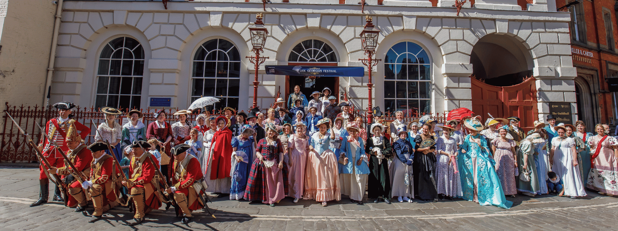 Participants in Georgian-era costume pose outside York Guildhall during the York Georgian Festival.