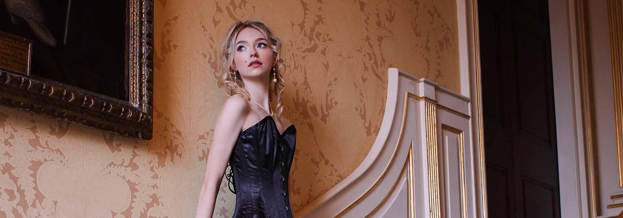 A lady in a corseted dress poses on a stair case.