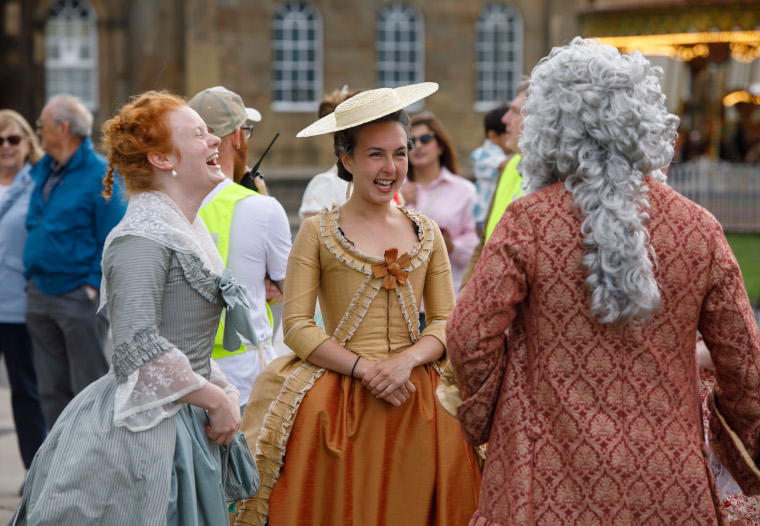 Two ladies in Georgian costumes laugh at a man in Georgian costume