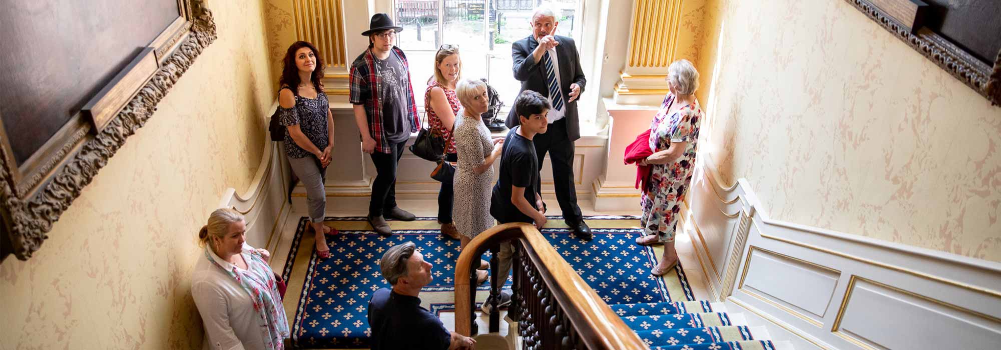 A group of visitors stand on a staircase and listen to a volunteer explain something