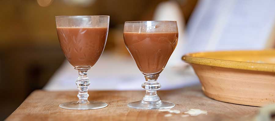 Two glasses filled with a dark coloured liquid sit on a chopping board