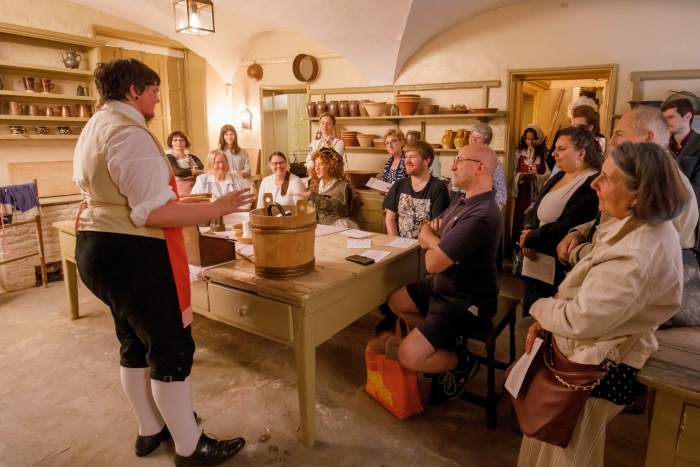 A group of sitting people gathered around a workbench, with a man on the left giving a speech to them